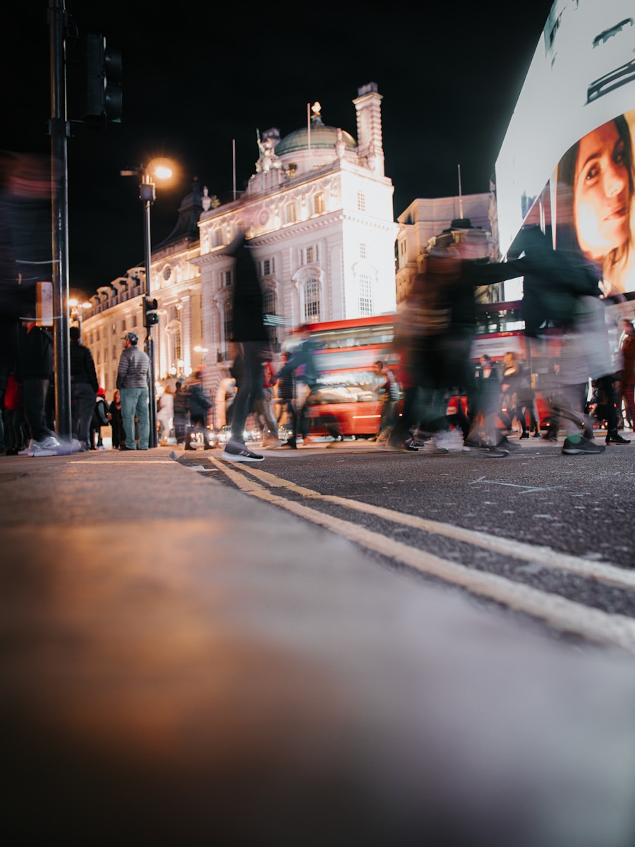 Blurred figures crossing a street at night with bus.